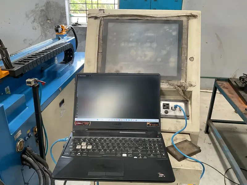A laptop connected by a blue Ethernet cable to a machine's control panel